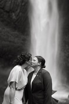 two women are kissing in front of a waterfall