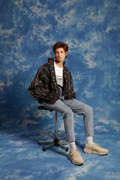 a young man sitting on top of a chair in front of a blue backdrop with clouds