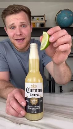 a man is holding an apple and a bottle of corona extra beer in front of him