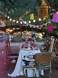 the table is set up for a tea party under a tree with paper lanterns hanging from it