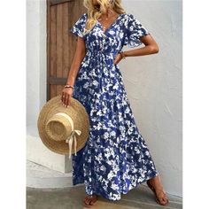 a woman wearing a blue and white floral print dress with a straw hat standing in front of a door