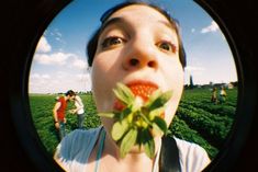 a woman holding a flower in front of her face and looking up at the sky