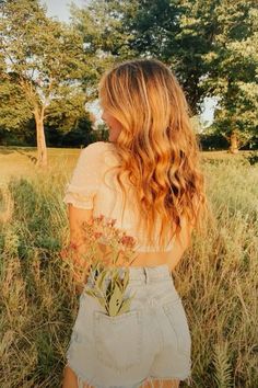 a woman with long hair standing in tall grass