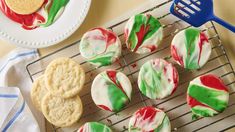 cookies decorated with green, red and white icing are on a cooling rack next to a fork