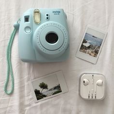 an instax camera sitting on top of a bed next to ear buds