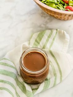 a jar of chocolate peanut butter next to a bowl of salad on a white table