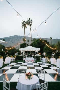 an outdoor wedding reception setup with white and black checkerboard flooring, lights strung over the tables