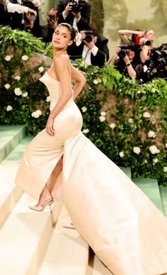 a woman in a white gown standing on steps with cameras around her and taking pictures