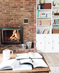 an open book sitting on top of a wooden table next to a fire in the fireplace