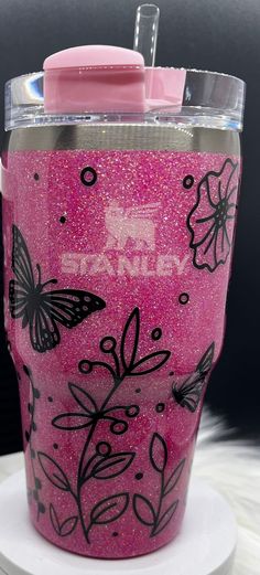 a pink tumbler with black butterflies and flowers on the lid is sitting on a white plate