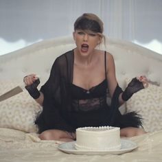 a woman sitting on a bed with a knife in her hand and a cake in front of her