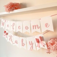 pink and white welcome baby banner hanging on the wall next to vases with flowers