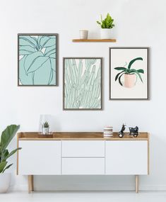 three framed art pieces hang on the wall above a white dresser with two plant pots