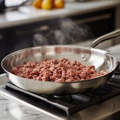 a frying pan filled with meat cooking on top of a gas stove next to an oven