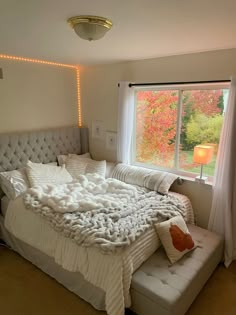 a bedroom with a large bed covered in blankets next to a window filled with fall leaves