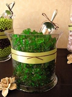 green candies are in glass containers with spoons and flowers on the table next to them