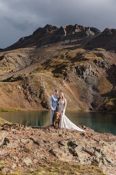 a bride and groom standing on top of a mountain with their dog in front of them