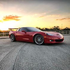 a red sports car parked on the side of a road in front of a sunset