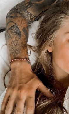 a woman laying in bed with tattoos on her arm and hand next to her face