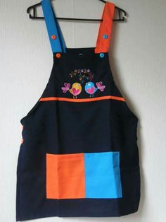 a child's apron hanging on a wall with an orange, blue and black patchwork design