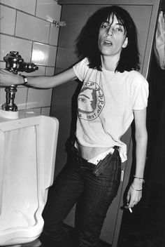 a woman standing in front of a urinal with her hand on the side of it