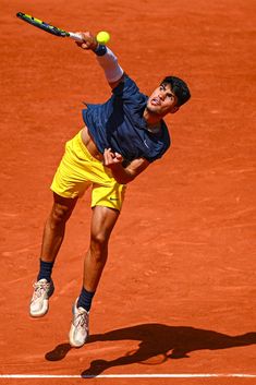 a tennis player in mid air after hitting the ball with his racket on a clay court