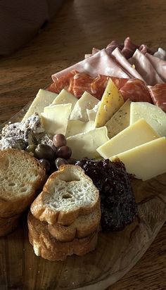 an assortment of cheeses and crackers on a wooden platter with bread slices