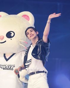 a man standing next to a giant teddy bear on stage with his arms in the air