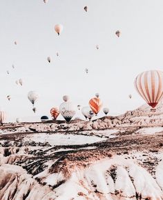 many hot air balloons are flying in the sky over some mountains and deserts, with snow on the ground