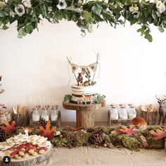 a table topped with lots of food and desserts next to a wall covered in greenery