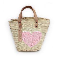 a straw bag with a pink heart painted on the front and tan leather strap around it