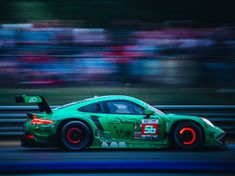 a green sports car driving on a track with blurry people watching from the stands