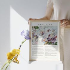 a woman holding up a framed poster with flowers in front of her