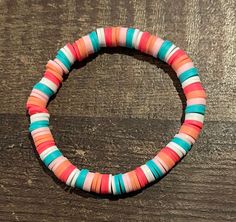 a bracelet made out of multicolored paper beads sits on a wooden table top