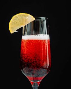 a wine glass filled with liquid and a lemon wedge on the rim, against a black background