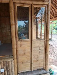 a bamboo hut with glass doors and windows on the outside, next to a trash can