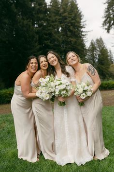 four bridesmaids pose for a photo in the grass with white flowers and greenery