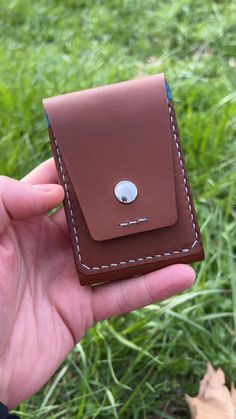 a hand holding a brown leather case with a button on the front and back side