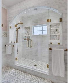 a bathroom with white tile and gold accents on the shower door, windows, and rugs