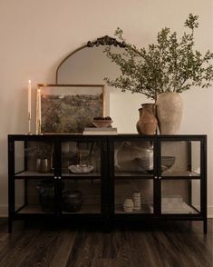 a glass cabinet with vases and plates on it in front of a mirror that is above the table