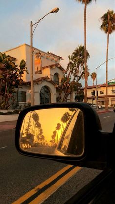 palm trees are reflected in the rear view mirror of a car