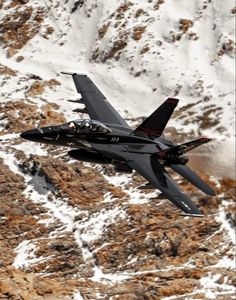 a fighter jet flying over a snow covered mountain