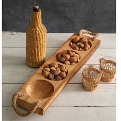 a wooden tray with nuts in it next to two glasses and a bottle on the table