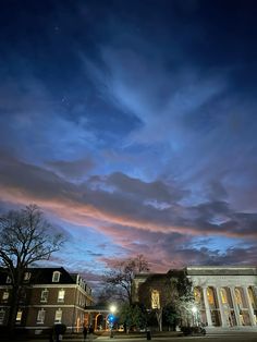 the sky is lit up at night with clouds and buildings in the foreground,