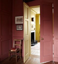 an open door leading to a living room with pink walls and wood floors, in front of a fire place