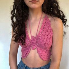 a woman wearing a pink crochet top and denim shorts with her hands on her hips