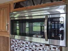 a stainless steel microwave oven in a kitchen with wooden cabinets and tile backsplash