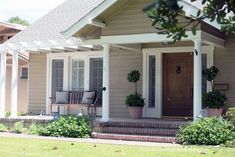 the front porch of a house with potted plants on the steps and two chairs outside