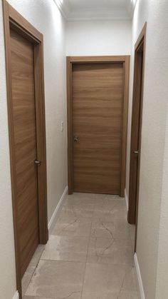 an empty hallway with two wooden doors and tile flooring on either side of the door