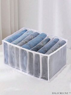 six pairs of jeans hanging in a clear storage bin on a white table with curtains behind it